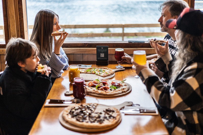 Una familia disfrutando de pizzas y jugos naturales en un restaurant con vista al río, el mejor panorama familiar en Cochamó.